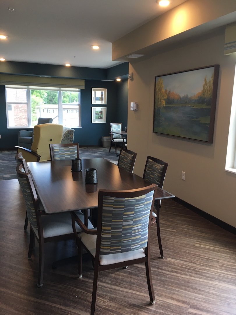 Modern dining area with a wooden table, six chairs, painting on wall, and windows in the background