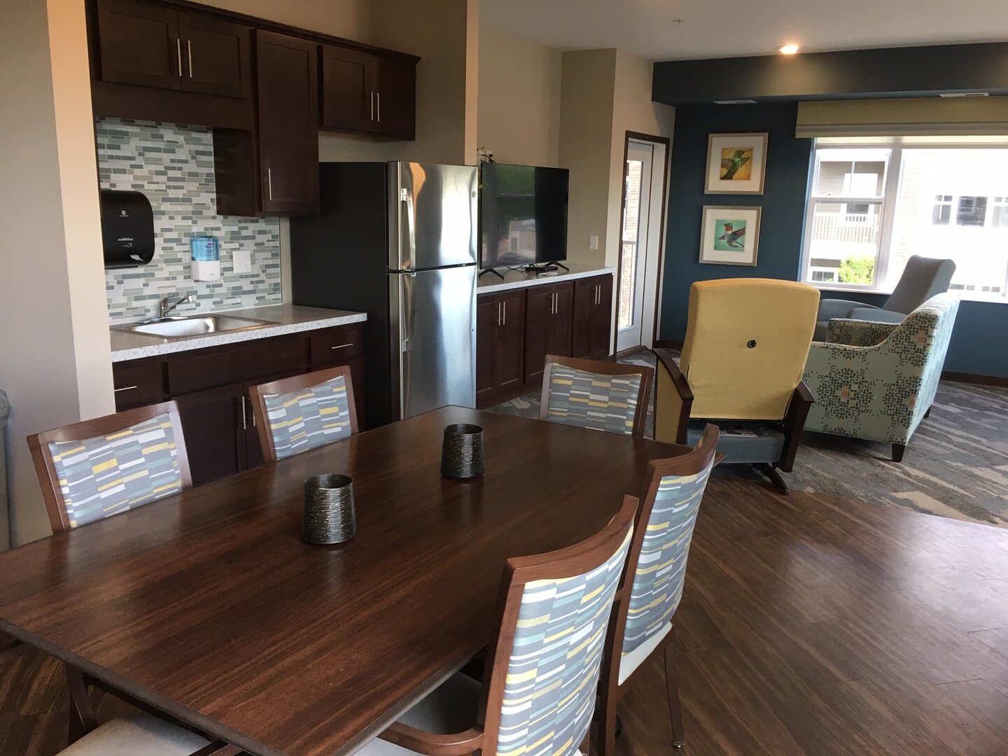 Modern communal area with dining table, kitchenette, and lounge chairs in a living community.