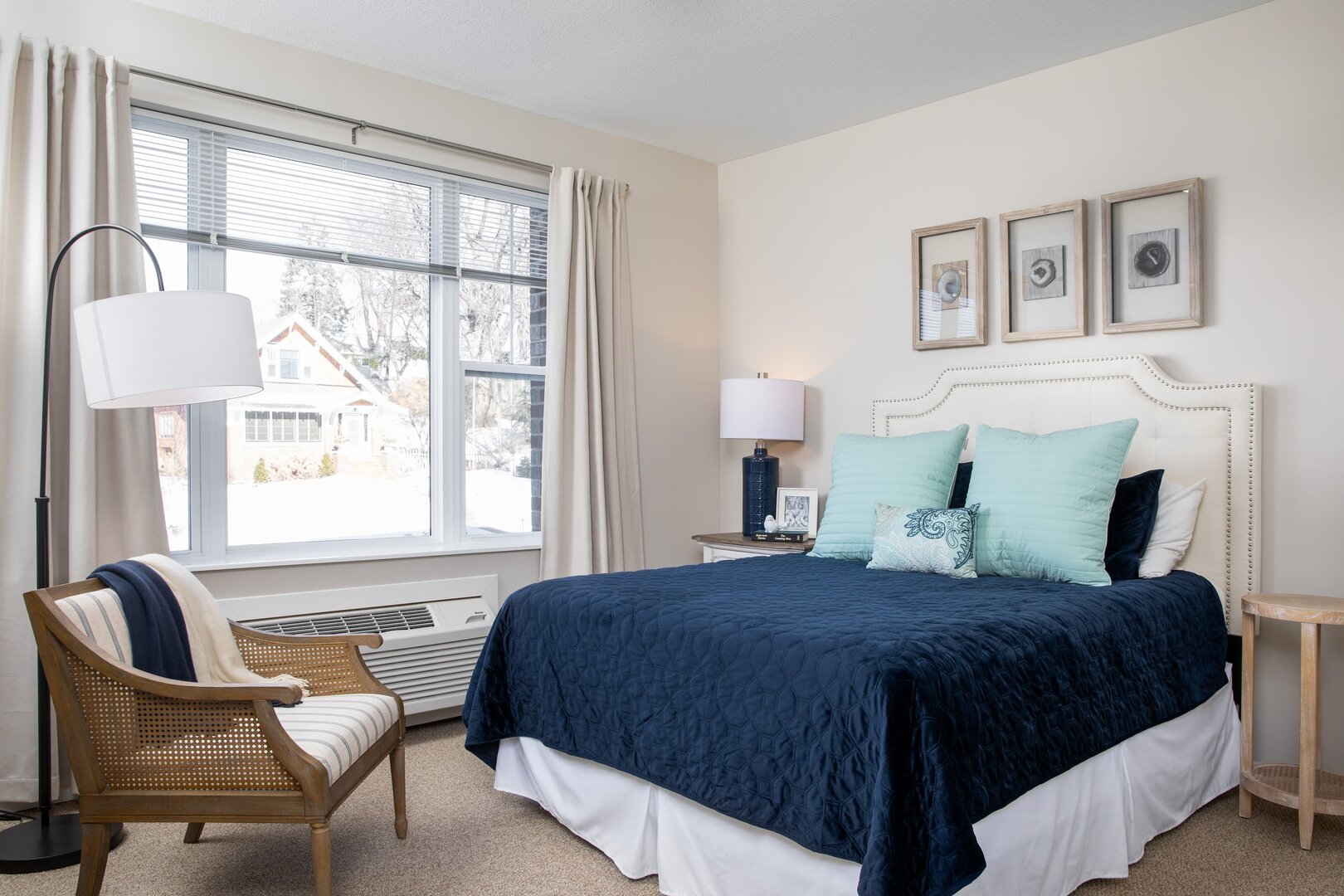 Bright bedroom with navy bedspread, large window, chair, and modern decor in senior unit.