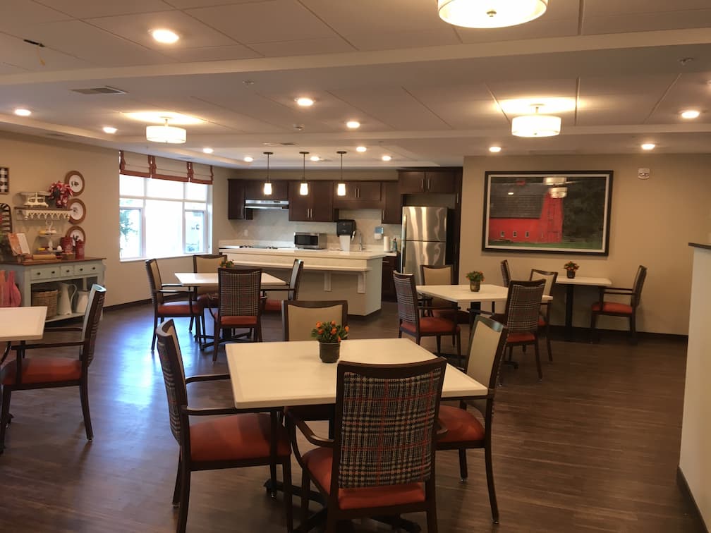 Dining area in a senior living community with tables, chairs, and modern kitchen.