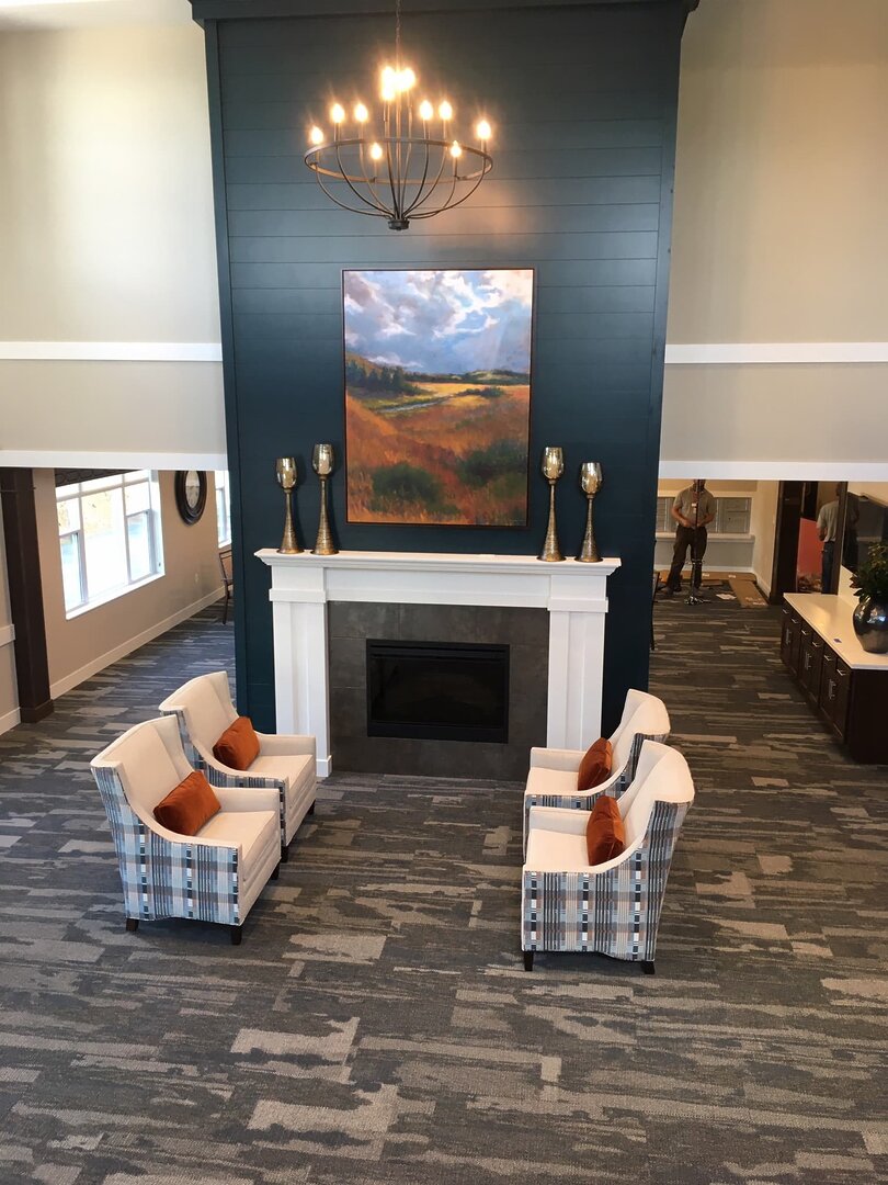 Elegant lounge area with armchairs, fireplace, and chandelier in living community.