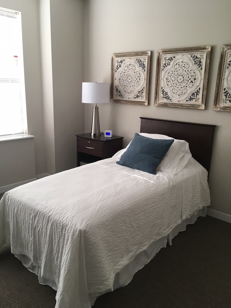 Cozy single bed with white linens in a well-lit unit with elegant decor.
