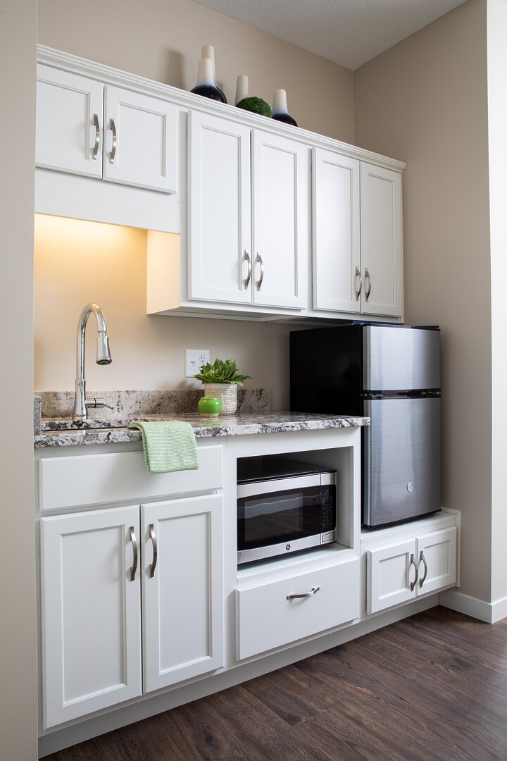 White kitchenette with cabinets, fridge, microwave, and sink with decor items.